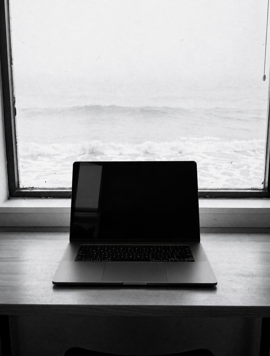 Laptop on a desk in front of a window looking out at the ocean